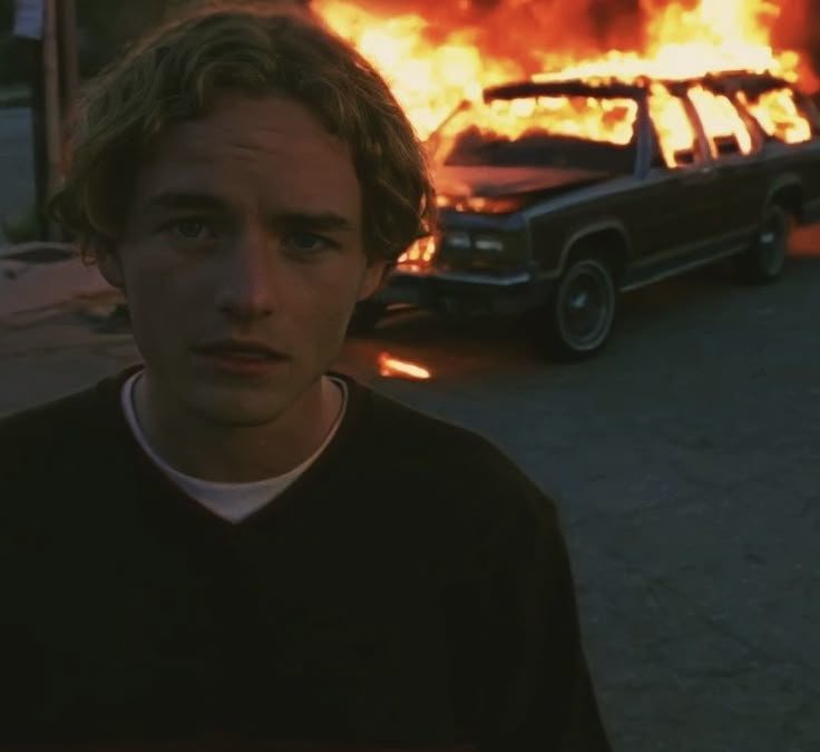 a young man in front of a car on fire