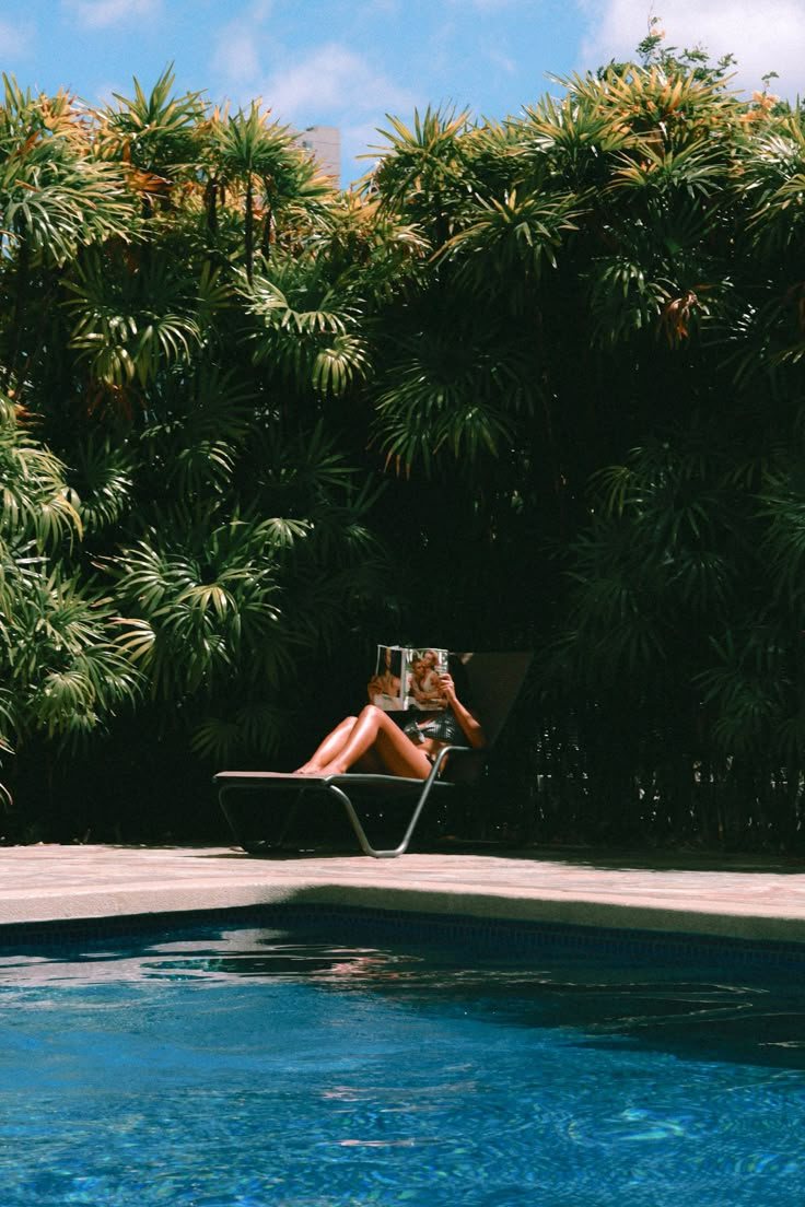 a woman sitting in a lawn chair next to a swimming pool